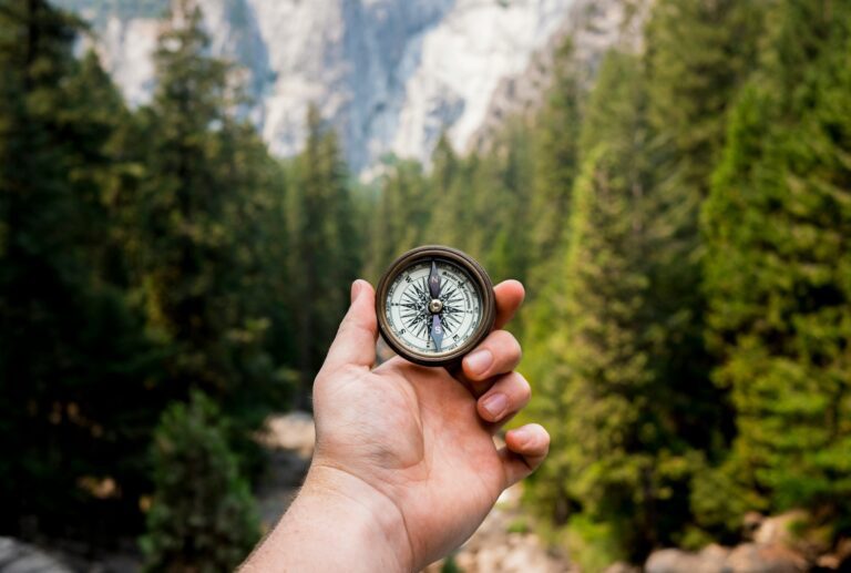 Person holding a compass with mountains in the background, symbolizing guidance and finding one’s core values.
