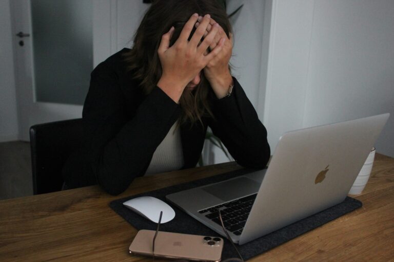 Woman working at a desk, face in her hands, clearly experiencing stress because of having to deal with a narcissistic boss.