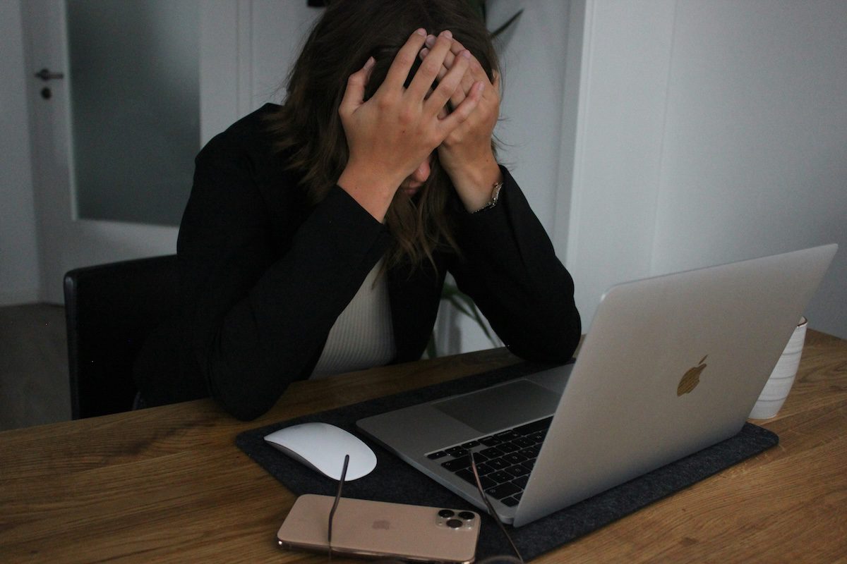 Woman working at a desk, face in her hands, clearly experiencing stress because of having to deal with a narcissistic boss.