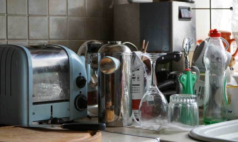 A cluttered kitchen countertop with scattered dishes, appliances, and glasses, creating a sense of overwhelm and household mess.