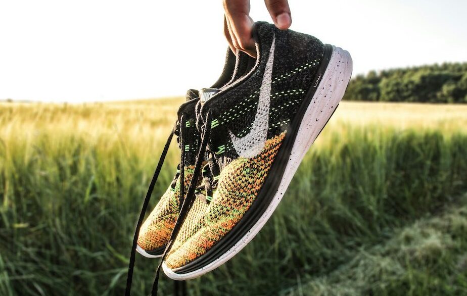 Hand holding a pair of worn running shoes in a sunlit field, symbolizing stepping back from overtraining and finding balance again.