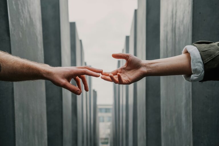 Two hands reaching toward each other in a narrow walkway, symbolizing human connection and the small moments that bridge isolation