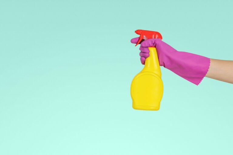 Person holding a yellow cleaning spray bottle with a pink glove, symbolizing simple cleaning habits.