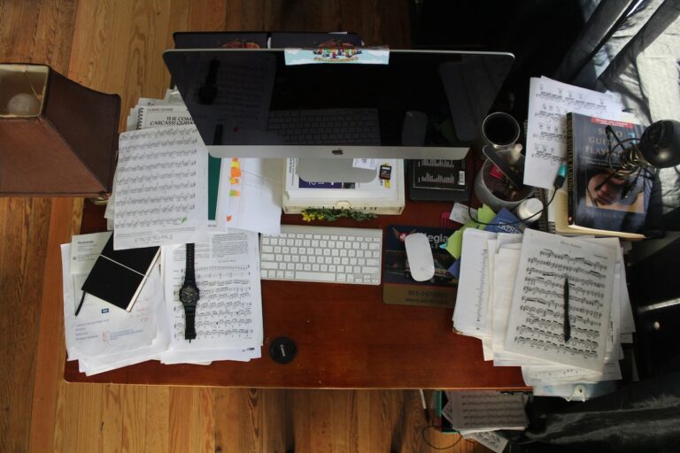 Overhead view of a cluttered work desk covered in papers, notebooks, and scattered objects, illustrating mental overload and fractured attention.