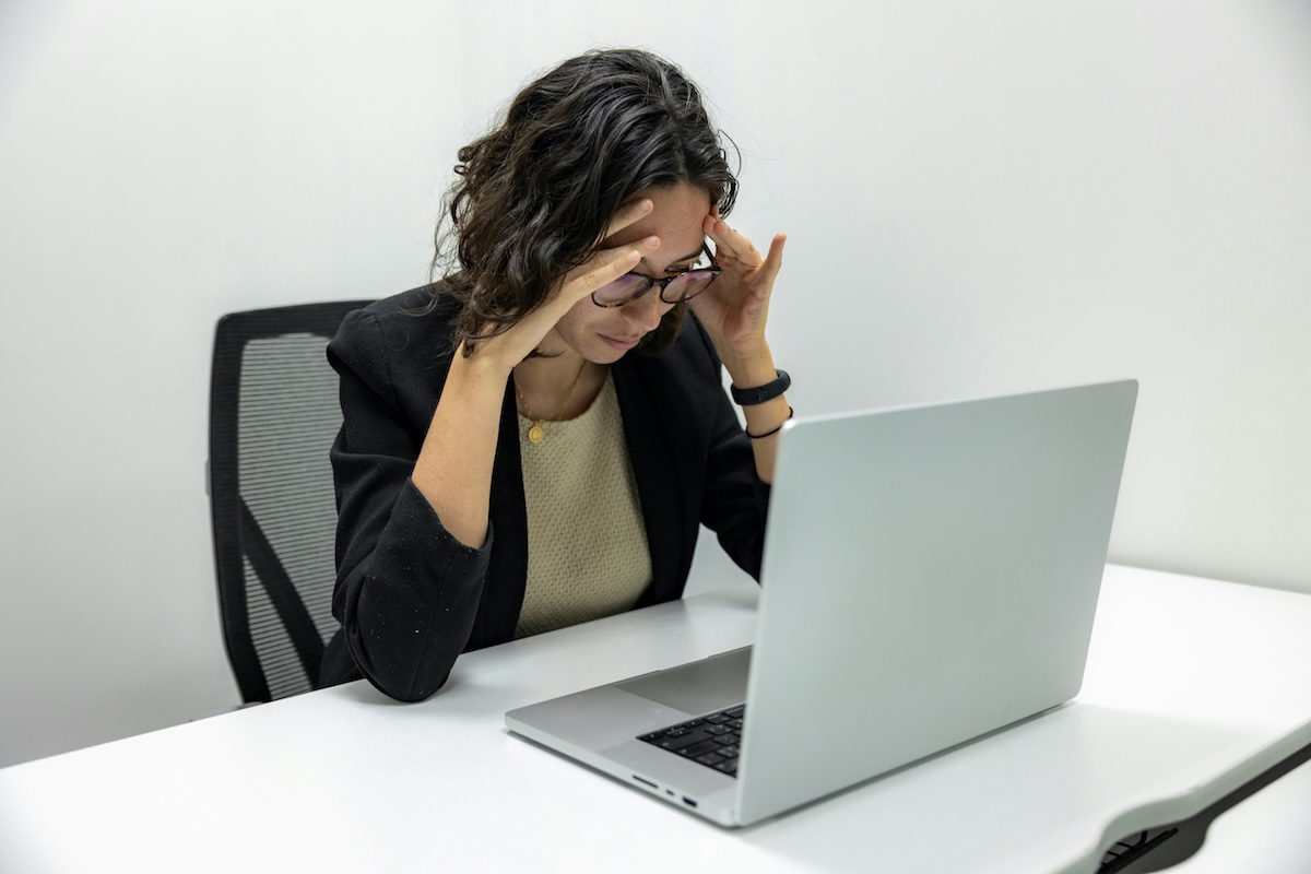 “Woman looking stressed while reviewing finances on a laptop at a desk”